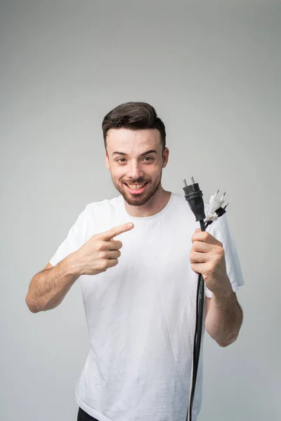Young man isolated over background. Cheerful positive guy hold cord with socket in hand and point on it. Master ready to repair socket. Vertical picture of handsome positive master. — Stock Photo, Image