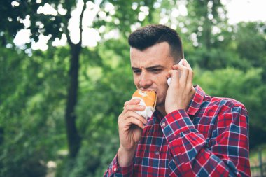 Otomatik sandviç yiyen yakışıklı genç adam. Elinde bir telefon var.
