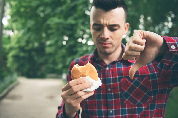 Man öppnar en hamburgare. Människan äter i parken — Stockfoto