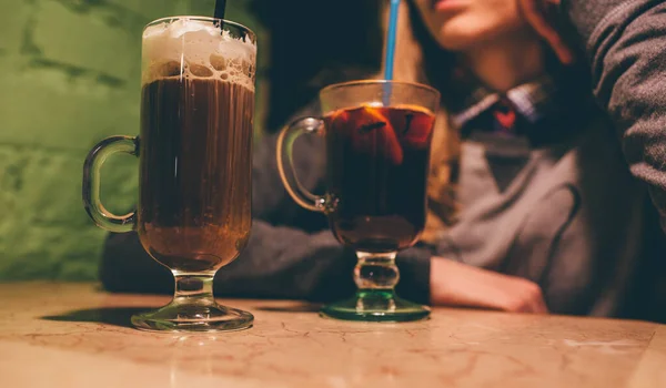 Vista de corte da mulher sentar-se na mesa. Latte com chantilly e vinho quente em copos. Senta-te no bar. pequeno café escuro sozinho. Coloque palha de plástico em vinho quente. Relaxe e hora do café . — Fotografia de Stock