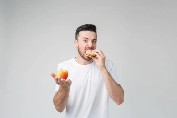 남자 애가 사과 랑 햄버거를 먹어요 남자가 햄버거를 먹는데그걸 안 좋아 해요. 그는 손가락을 아래로 보여. 남자 아이는 당근을 먹어 — 스톡 사진