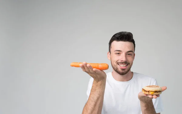Chico come una zanahoria y hamburguesa. El hombre hace la elección entre comida rápida y saludable. Sabroso o útil El dilema de elegir un estilo de vida diferente — Foto de Stock