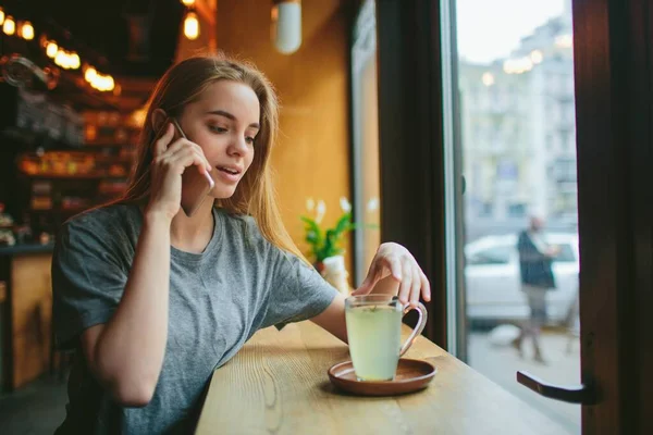 Sarışın telefonu kullanıyor. Kız ve akıllı telefon. Kafede cep telefonu olan bir kadın oturuyor.. — Stok fotoğraf