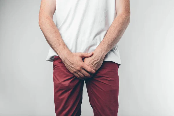 Caucasian man in white T-shirt and burgundy pants. Holds his hands on groin. Cut view. Concept. Isolated over light background. — Stock Image Caucasian man in white T-shirt and burgundy pants. Holds his hands on groin. Cut view. Concept. Isolated over light background. Stock Photo