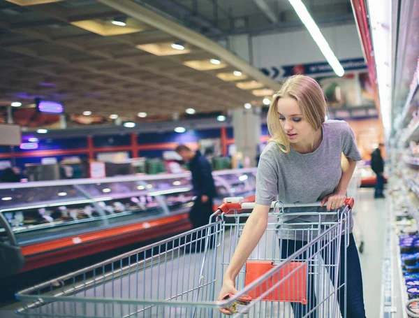 Curious Woman in The Supermarket . Young girl in a market store with shopping thinking what to buy