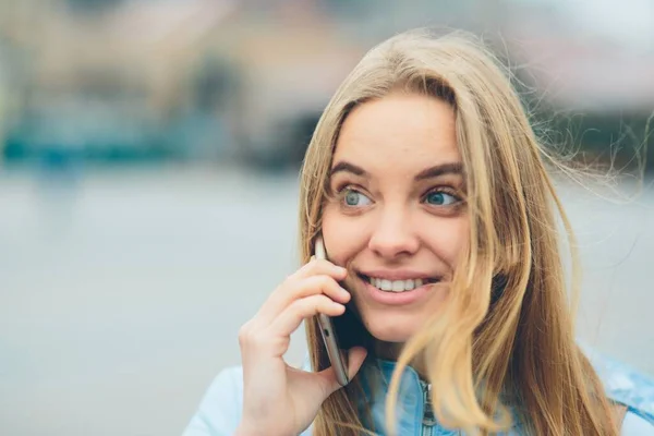 Loira linda emocional falando ao telefone ao ar livre. Feminino Rostos corruptos e se entrega a conversar com amigos no celular . — Fotografia de Stock