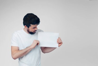 Genç adam arka planda izole edilmiş. Beyaz gömlekli esmer, boş sayfayı tut ve bak. Stüdyoda yalnız. İki elinle tut..