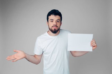 Genç adam arka planda izole edilmiş. Elinde boş bir sayfayla kameraya poz veren tuhaf, duygusal bir adam. Ne yapacağını bilemiyor..
