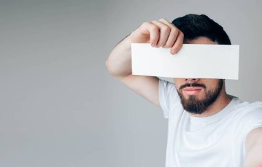 Genç adam arka planda izole edilmiş. Yan görünüş ve sakallı adamın selfie 'si gözleri kameradan gizliyor. Bir parça kağıt ya da sayfayı elinizde tutun