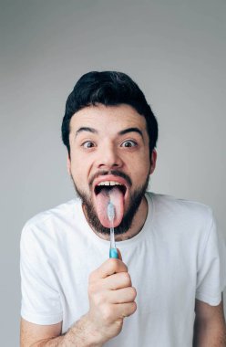 Genç adam arka planda izole edilmiş. Kamerada poz veren heyecanlı pozitif adam. Üzerinde diş fırçası ve diş macunu olan bir dil göster. Sağlık sigortası konsepti. Ağız tedavisi