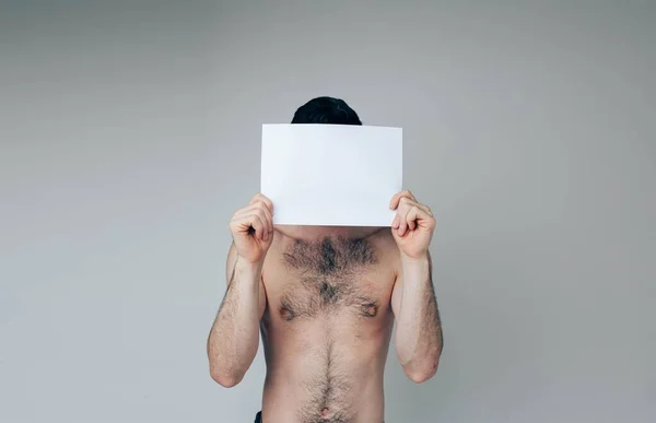 Νεαρός απομονωμένος στο παρασκήνιο. Γυμνός συνηθισμένος τύπος καλύπτει το πρόσωπο με λευκή λευκή σελίδα. Κρύψε κάποιον. Απόσπαση στην κάμερα — Φωτογραφία Αρχείου