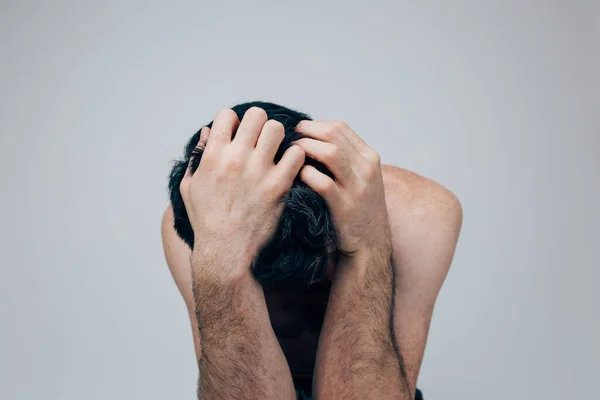 Jeune homme isolé sur fond. Un émotif stressé se cachant face contre terre et le couvrant de ses mains. Homme avec malaise, confusion et maladie. gars confus sur la photo . — Photo