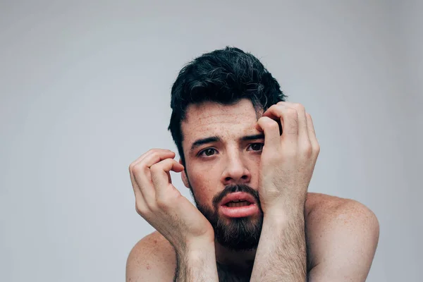 Junger Mann isoliert über Hintergrund. Müder kranker trauriger Kerl schaut in die Kamera. Berühren Sie Gesicht mit den Händen. Gestörter Typ mit Gehirnkrankheit. Stressig und krank. — Stockfoto