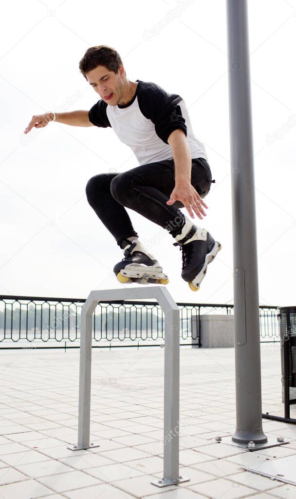 Picture of professional young man jumping during rollers skating outside on street. Urban view. Skating with obstacle. Jump up. Daylight.