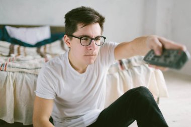 Evdeki yatakta otururken uzaktan kumanda kullanan adam. Televizyon izleyen mutlu, çekici bir genç adam. Yüzünde insani duygular.