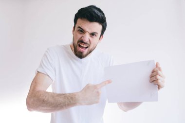 Beyaz bir kağıt parçası tutan sakallı bir adam. Kızgın genç adam kameraya parmaklarını gösteriyor..