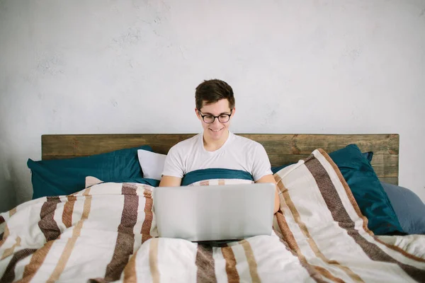 Casual young man using laptop in bed at home — Stock Photo, Image