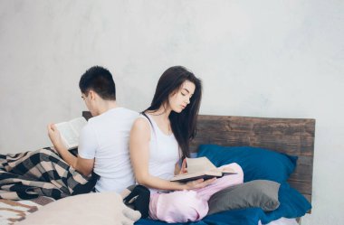 Genç bir adam ve kadın yatakta oturup kitap okuyorlar. Evde romantik bir sabah.