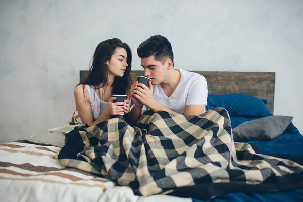 Ein junger Mann und eine Frau trinken morgens im Bett Kaffee. Romantischer Morgen zu Hause — Stockfoto