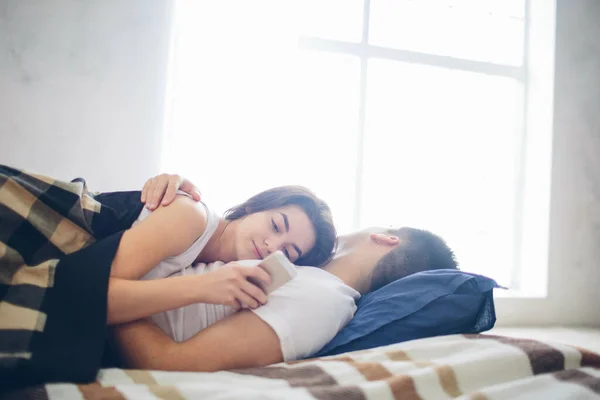 Ein Liebespaar liegt auf dem Bett. Eine Frau benutzt ein Smartphone — Stockfoto