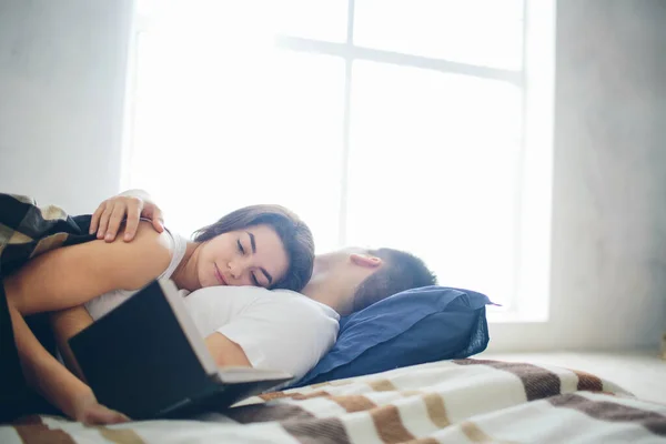 Um casal amoroso está deitado na cama. Mulher está lendo um livro — Fotografia de Stock