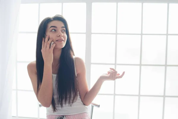 Jeune femme parlant au téléphone à la fenêtre dans sa maison . — Photo