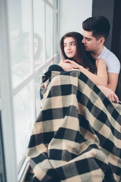 Ein Liebespaar liegt an einem Fenster, das in Sonnenlicht getaucht ist. Helles und gemütliches Schlafzimmer. Komfort und Liebe in der Familie — Stockfoto