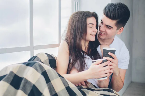 Ein junger Mann und eine Frau trinken morgens im Bett Kaffee. Romantischer Morgen zu Hause. — Stockfoto