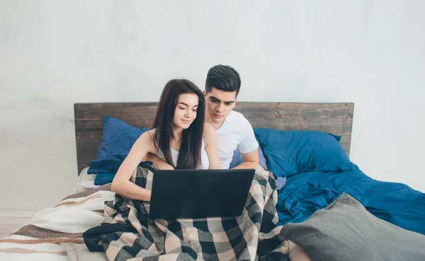 Hombres y mujeres jóvenes están trabajando en el ordenador o en busca de información sobre el Internet en la cama . — Foto de Stock