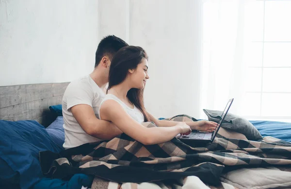 Hombres y mujeres jóvenes están trabajando en el ordenador o en busca de información sobre el Internet en la cama . — Foto de Stock