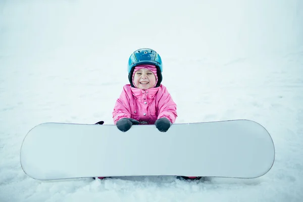 Snowboard Kış Sporu. Karla oynayan küçük bir kız. Sıcak kışlık giysiler giyiyor.. — Stok fotoğraf