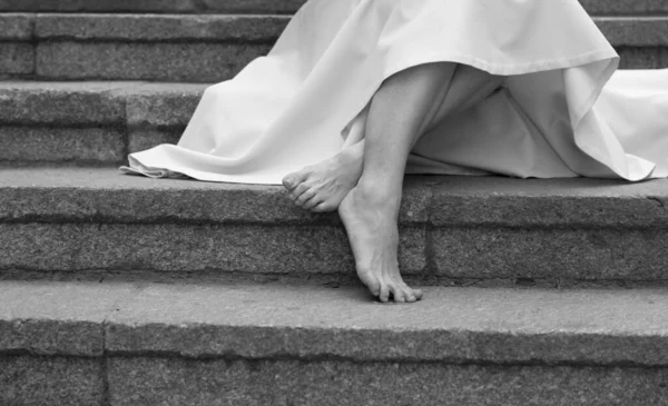 Attraktiv smal barfota ben och fötter av ung kvinna i klänning på bild. Kvinnlig modell sitter på stepa och posinf. Ensam utanför på trappan. Höger ben fram. — Stockfoto