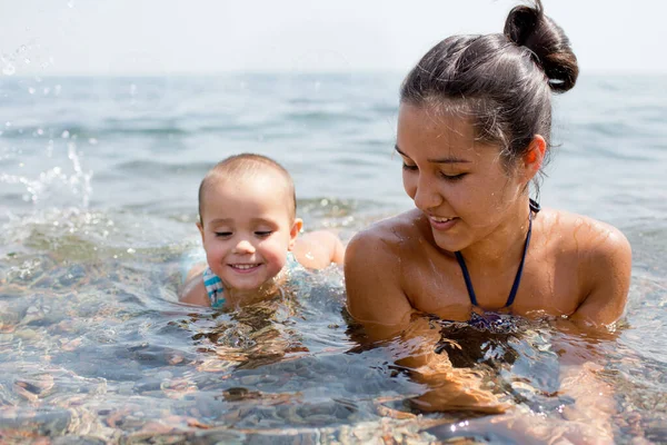 Young woman and small child swimming in ocean or river by coastline or beach. Mother teches daughter hot to swim. Happy child playing in water. Daylight. Royalty Free Stock Photos