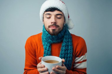 Arka planda izole edilmiş genç sakallı adam. Elinde beyaz bardakla ve gözleri kapalı sakin sakin bir adam. Eşarp boynunda. Kış kıyafetlerini giy. Noel ve yeni yıl havası.