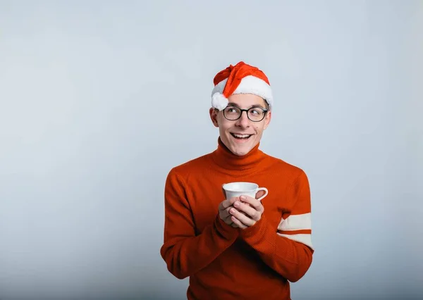 Jonge gelukkige kerstman in rode kleren en hoed die warme drank drinkt van een witte mok. Kerst en nieuwjaar. Geïsoleerd boven de achtergrond. — Stockfoto