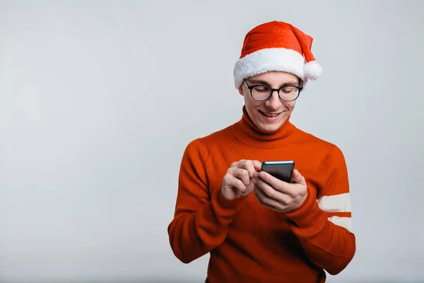 Happy handsome man in christmas hat looks at his smartphone — Stock Photo, Image