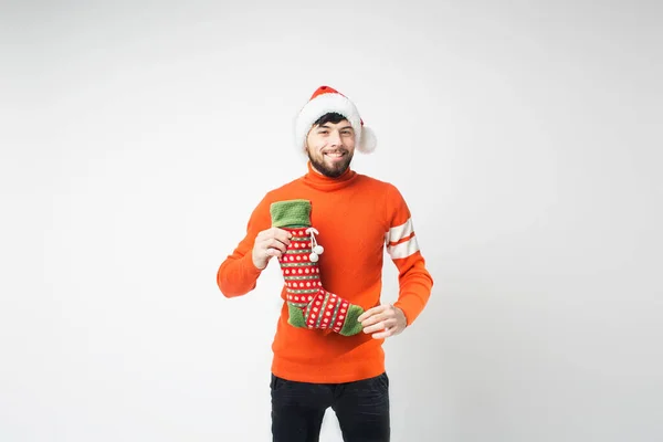 Jeune homme barbu isolé sur fond. Le gars se tient en tenue rouge et pose. Temps de Noël et nouvel an humeur. Tenez chaussette pour cadeaux . — Photo