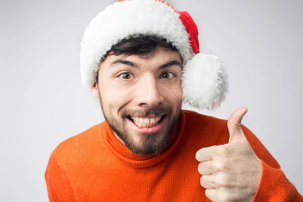 Young bearded man isolated over background. Positive guy hold big thumb up. Portrait of man in Christmas clothes and hat. Alone in studio. — Stock Photo, Image