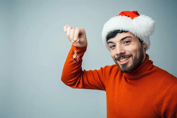 Young bearded man isolated over background. Cheerful positive guy hold small chistmas tree decoration in hand and show it. New year clothes, style and mood. — Stock Photo, Image