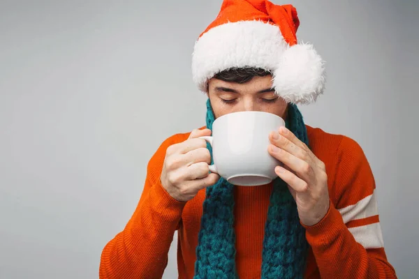 Young bearded man isolated over background. Drink coffee or tea from white cup. Wear Christmas or new year clothes. Black haired Santa. — Stock Photo, Image