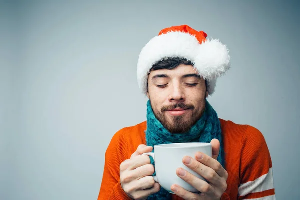 Young bearded man isolated over background. Satisfied peaceful dark haired guy enjoy drinking from white cup. Get warmth in cold day. Wear red Santas clothes. — Stock Photo, Image