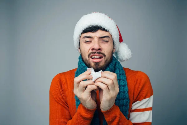 Young bearded man isolated over background. Guy in red festive clothes and hat suffer from running nose. Sneezing and caughing. Alone in studio. — Stock Photo, Image