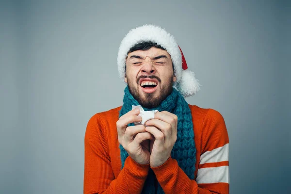 Young bearded man isolated over background. Picture of guy sneezing and read to do it in napkin. Man in red lcothes and hat during holidays time. Christmas or new year. — Stock Photo, Image