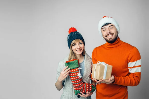 Jeune homme barbu et femme gaie isolé sur fond. Tenez-vous ensemble dans des vêtements de Noël de fête. Tenez aock et cadeau o présent dans les mains. Poser ensemble . — Photo