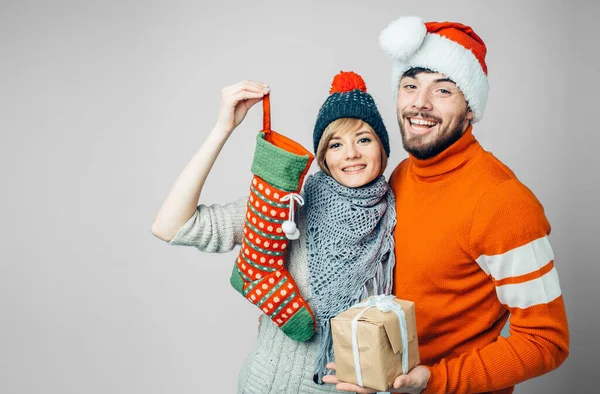 Jeune homme barbu et femme gaie isolé sur fond. Elle tient dans ses mains une chaussette de fête. Il a un cadeau ou un cadeau. Poser ensemble sur la caméra . — Photo