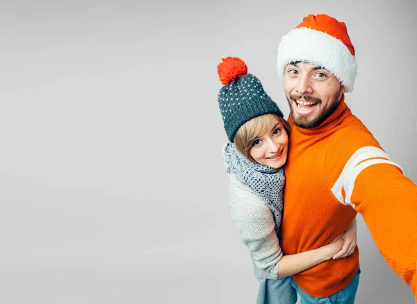 Jeune homme barbu et femme gaie isolé sur fond. Selfie de couple ou de famille posant ensemble. Il tient la caméra et sourit. Les deux portent des vêtements de Noël. Nouvel an ambiance festive . — Photo