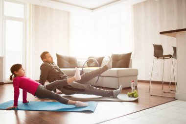 Baba ve kızı evde antrenman yapıyorlar. Apartman dairesinde egzersiz. Evde spor haberleri. Tahtayı ters çevirin ve evdeki zeminde bacak yükseltin.