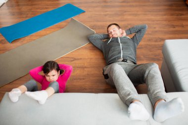 Baba ve kızı evde karın kası eğitimi yapıyorlar. Apartman dairesinde egzersiz. Oturma odasında spor eğitimi var.