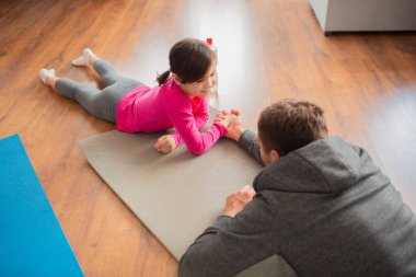 Baba ve kızı evde antrenman yapıyorlar. Apartman dairesinde egzersiz. Evde spor haberleri. Bilek güreşi yap ve yoga minderine uzan.