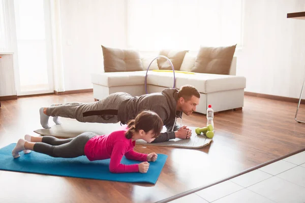 Padre e hija están entrenando en casa. Entrenamiento en el apartamento. Deportes en condiciones de casa. Hacen la tabla de hacer . — Foto de Stock